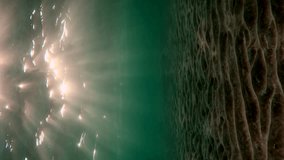 Vertical video, Low angle wide shot sun rays penetrating surface of water lie on sandy bottom at sunset. Slow motion, Underwater light creates beautiful veil, consisting of sunlight at evening light