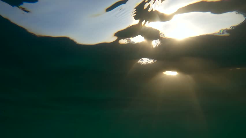 Last rays of setting sun penetrate water surface of water, Slow motion. Sunlight undersea at sundown. Natural underwater background with sunbeams at sunset time, Evening sunburst below surface of sea