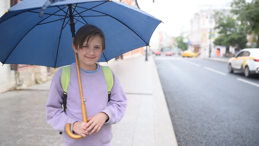 A 10-year-old boy with an umbrella stands in the rain at a bus stop, waiting for transport, a bus.