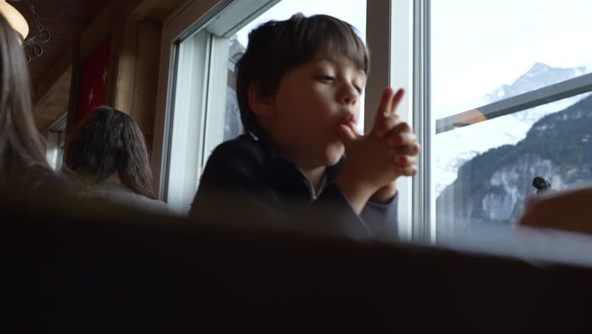 Little boy pretending to shoot a pistol with hands while waiting for food to arrive at restaurant diner. Restless male child