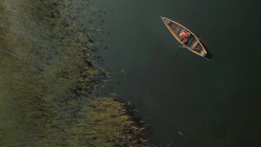Vertical video. Wooden boat with fisherman on the lake. Aerial view.