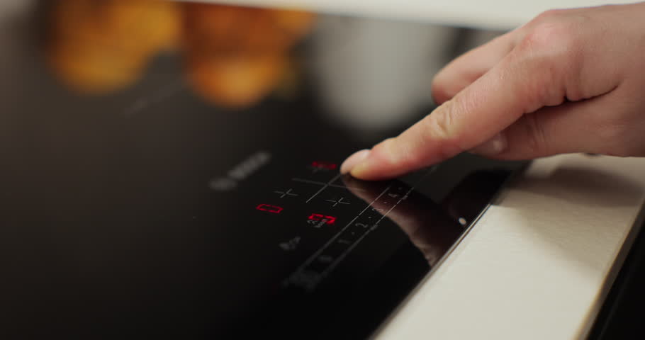 Woman hand turn on induction stove to cook. Finger touching sensor button on induction or electrical hob. Modern technology.