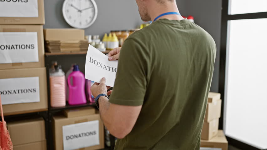 A man in a warehouse organizing donation boxes labeled for charity with a focus on volunteer work, highlighting compassion and community service. Royalty-Free Stock Footage #3410367999