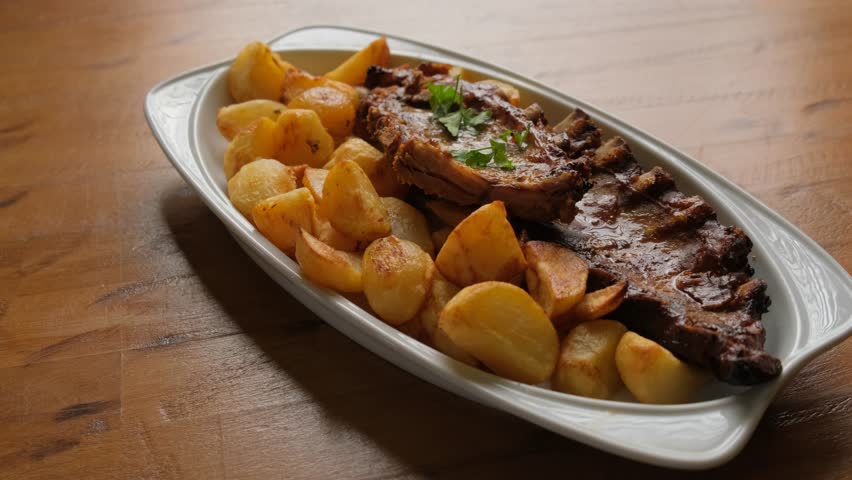 A dish of potatoes and pork ribs on a wooden table close-up.