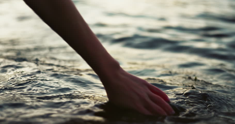 Closeup, hand and water in morning by sea with touch, waves and nature on vacation in sunshine. Person, fingers and outdoor vacation by river, lake and ocean in environment with ripple in Japan