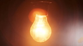 Hanging on wire incandescent bulb turns on, and off and flickers on black background, place for text. Warm flashing filament close-up. Glass old bulb glowing yellow warm light. Tungsten lamp. Idea 4K - Powered by Shutterstock - Get 15% off with code: PIKWIZARD15