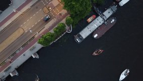 A clip of a drone hovering over a river and bridge while boats, cyclists and cars pass by underneath at the amstel river in amsterdam
