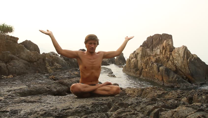 Young yoga man doing exercise on the deserted wild stone sea beach (HD) 