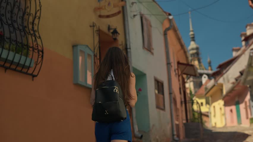 Young tourist woman walking on the empty colourful street of medieval old town Sighisoara in Transylvania during summer. Travel vacation concept in Romania Europe