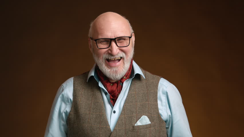 A middle-aged man stylishly dressed radiates joy and happiness with a joyful smile. He has a gray beard and is wearing a classic waistcoat with a neck scarf, standing against a brown background. Raw.