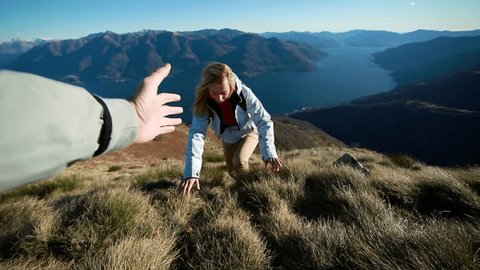Closeup of a male's hand stretching out and helping female hiker reach the mountain top by pulling her up. POV of a man giving hand to a woman climbing on the mountain and helping her reach the top