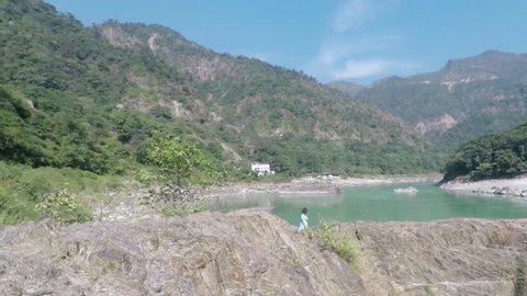 Caucasian Hindu woman walks up steps to Shiva Lingam, in Rishikesh, India. Hills, river and ashrams in background. Smooth tracking. Wide. 2X slow motion.