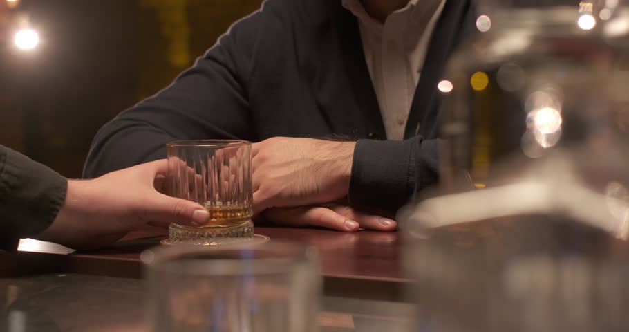 Bartender puts a glass whiskey on the bar serving customer in pub. Man resting with glass of whiskey at hotel lounge
