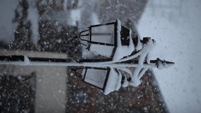 Heavy snowfall in winter. Lamppost cover of snow and ice. Little village in the mountain, french alps. Slow motion vertical video for reels. Blizzard, snow flakes, city street. Crest-Voland, France.