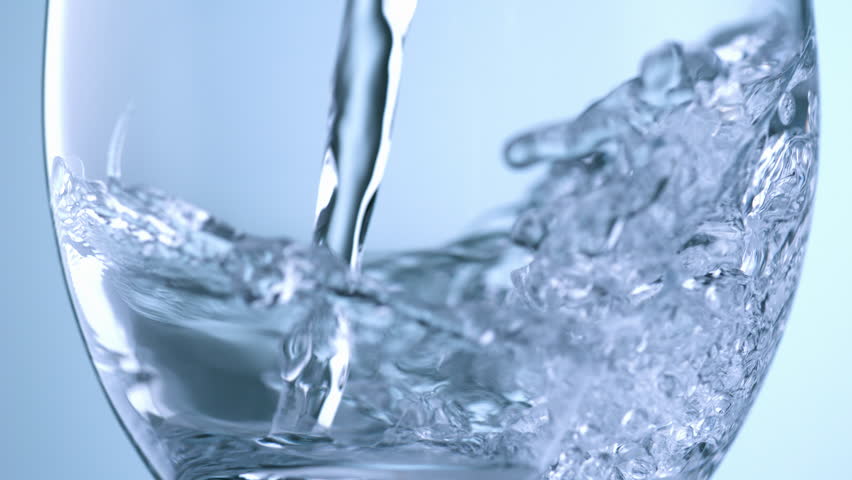 High speed shot close up of clear mineral water pouring into drinking glass