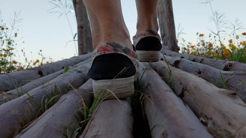 A woman in a long white dress, flowing fabric, walks on a bamboo bridge.  Steep and inclined