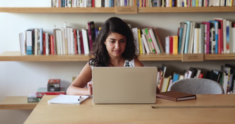 Young Indian woman studying on-line make research, e-learning looking focused sit at desk in university library. Businesswoman working on computer in office, typing e-mail, contact to client remotely Royalty-Free Stock Footage #3411170775