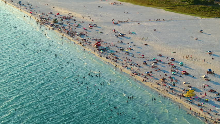 Famous Siesta Key beach with soft white sand in Sarasota, USA. Many people enjoing vacation time bathing in warm gulf water and tanning under hot Florida sun at sunset
