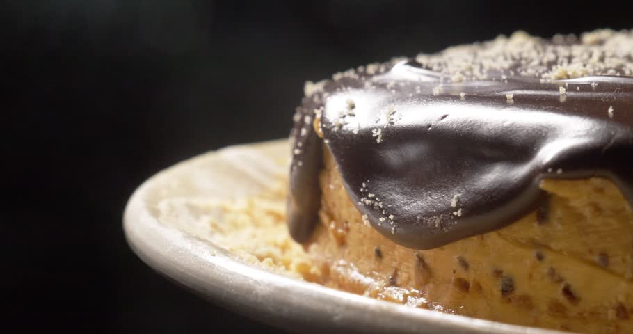 Festive homemade chocolate cake on a platter spinning on a black background close-up.