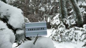 Subscribe message on a letter light box, placed on a pine branch covered in snow. Snowfall in a beautiful winter forest background. - Powered by Shutterstock - Get 15% off with code: PIKWIZARD15