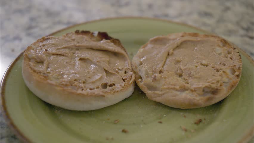 Drizzle and spread honey on a toasted English muffin with peanut butter on a green plate on a marble countertop Royalty-Free Stock Footage #3411514039