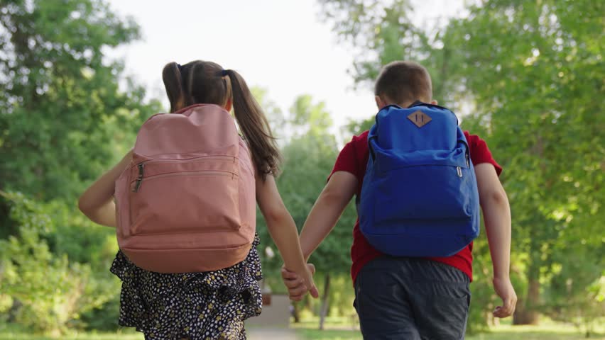 boy girl holding hands running through park school, child with school backpacks running along sidewalk school lesson, cheerful classmates running hand hand with bags, teamwork group children, boy girl