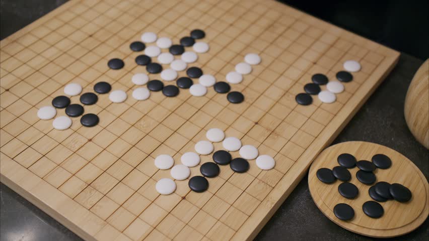 45 degree overhead angle of hand playing white stone in Go board game with tiles already on grid and black pieces in corner
