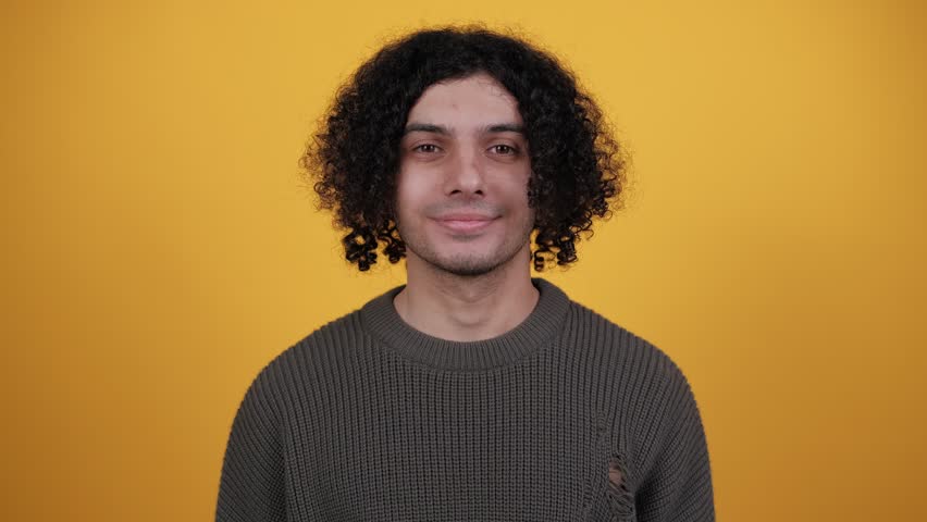 Positive curly man nodding head, say yes, showing approving gesture, body language concept. Indoor studio shot isolated on yellow background. People lifestyle concept