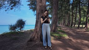 A woman stands and uses a cell phone under the shade of a pine tree.
Tunnel of pine trees along the blue sea beach.
Under the shade of a large tree. slow motion