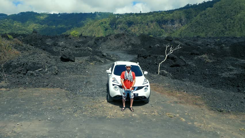 A man stands by a car in the middle of a frozen black lava field on a volcano. Aerial drone view.