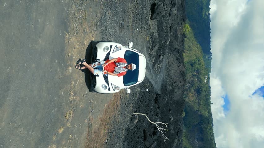 A man stands by a car in the middle of a frozen black lava field on a volcano. Aerial drone vertical view.