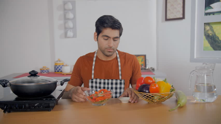 Indian home cook sprinkling salt on his tomato and cucumber salad - healthy food, vegetarian diet, vegan dish. Handsome man seasoning a delicious and nutritious meal - following a diet, healthy 