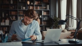 young man with beard in blue shirt sits at table in home office, multitasking with laptop, mobile phone, notebook, be in a hurry, stays focused under the pressure work deadlines. speed up - Powered by Shutterstock - Get 15% off with code: PIKWIZARD15
