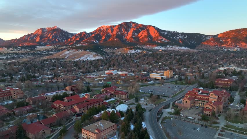 Drone flying over the University of Colorado Boulder (CU Boulder) at sunset on a winter morning. College campus with library and student housing in view.