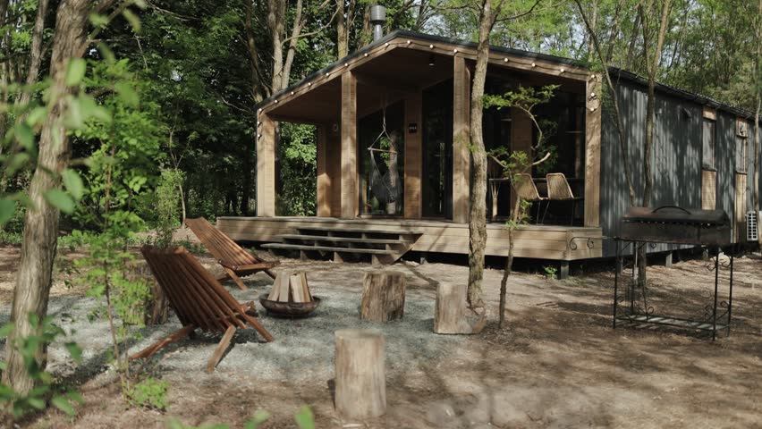 Wooden large cabin house, scandinavian house hidden in nature among the pine trees, two cozy wooden chairs and fireplace on the front of the house. slow motion.