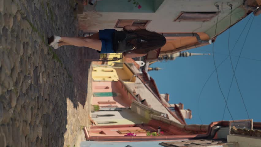 Vertical shot young tourist woman walking on the empty colourful street of medieval old town Sighisoara in Transylvania during summer. Travel vacation concept in Romania Europe