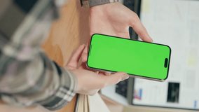 Close-up Of Mobile Phone With Vertical Green Screen In Female Hands. Girl Uses Smartphone In Office Or At Home