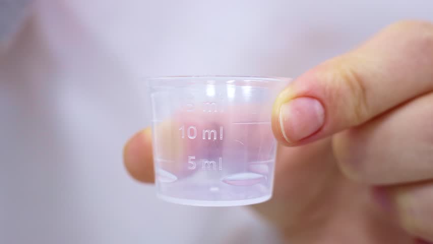 Female hands poring portion of liquid medicine syrup for treatment cough, cold and flu into measuring cup. Taking medicine, health care, pharmacy concept