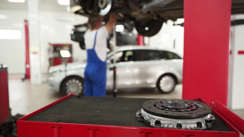 Auto mechanic installs new clutch in car. Workshop professional works on vehicle gearbox, replaces components like disc, cover, plate. Maintenance repair performed in garage setting.