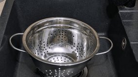 Short clip of freshly boiled spaghetti being drained off in the stainless steel strainer placed in the kitchen sink