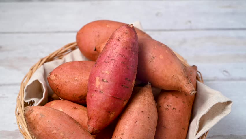 Whole raw sweet potatoes in a basket, on bright background, top view.