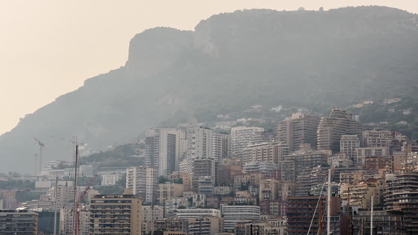 Residential complex of Monacoin the haze at sunset, buildings of different height against mountains, skyscrapers, clouds over city