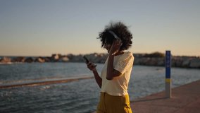 Video of a happy african woman dancing and singing listening to music with headphones next to the sea