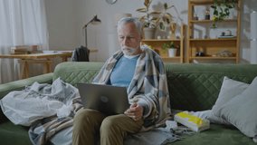 Elderly man sitting on sofa, making distant video call. Senior patient looking at laptop screen, communicating with doctor therapist online, asking how to take medicine
