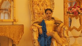 A woman in gold fantasy armor, fur, and a blue cape sits on an ornate, high-backed throne. She poses powerfully with stylized makeup, looking at the camera. - Powered by Shutterstock - Get 15% off with code: PIKWIZARD15