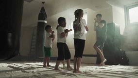 Children punch air following trainer in martial arts class. Junior sportsmen study attacking by hands with master in gym slow motion. Healthy kids - Powered by Shutterstock - Get 15% off with code: PIKWIZARD15