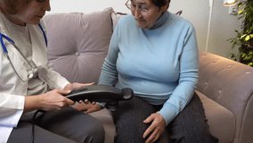 A family doctor massages an elderly woman's leg with an electric massager. Ideal for content about healthcare, elder care, and home health programs.