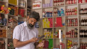 Close-up shot of kirana merchant busy on mobile phone at the grocery store - small business, shop next door, India. Indian shopkeeper taking online orders at his grocery store - online delivery, ph... - Powered by Shutterstock - Get 15% off with code: PIKWIZARD15