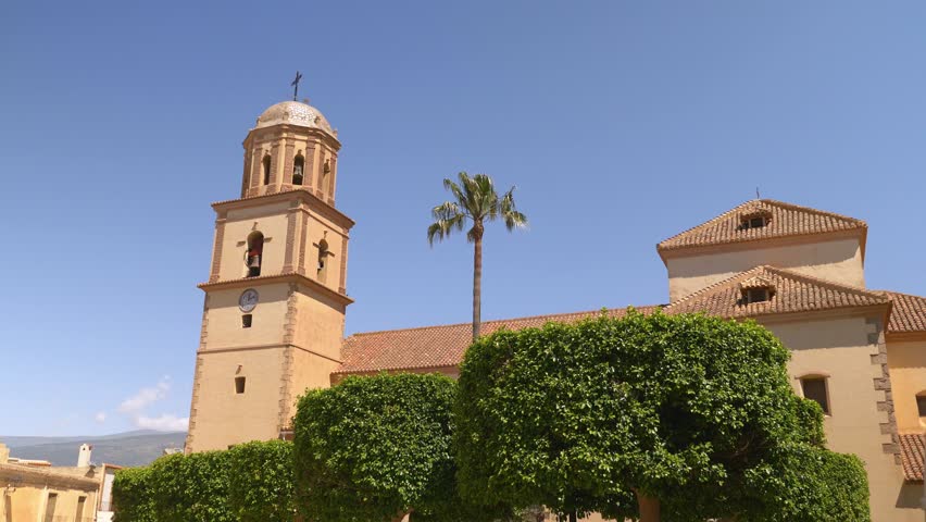 Church with tile roof behing green bushes and palm tree in summer in village of south of Spain, Europe