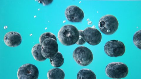 blueberries falling into water on blue background. Macro view
